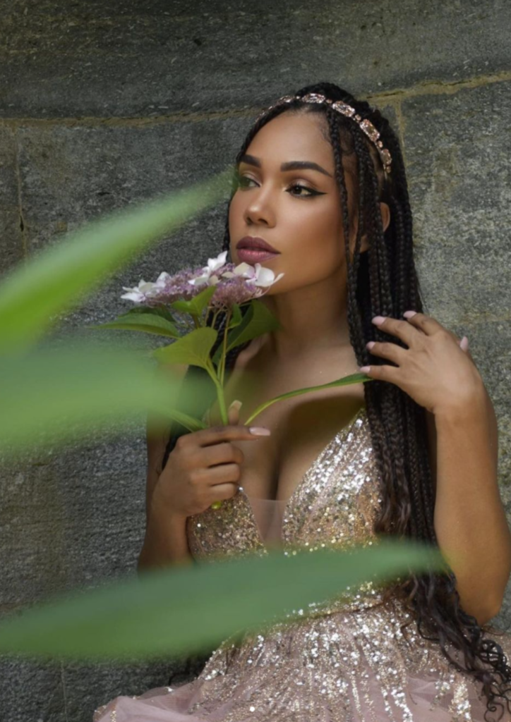 Woman with braids holding a flower, posing with a thoughtful expression.