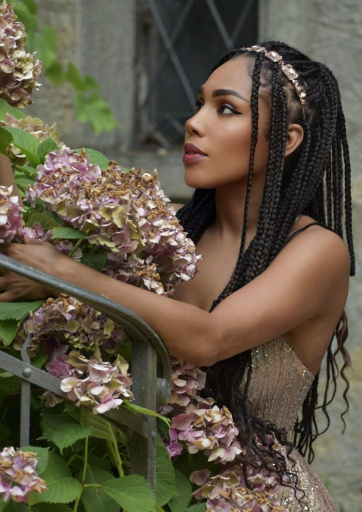 Woman with braids surrounded by dried flowers in a rustic setting.