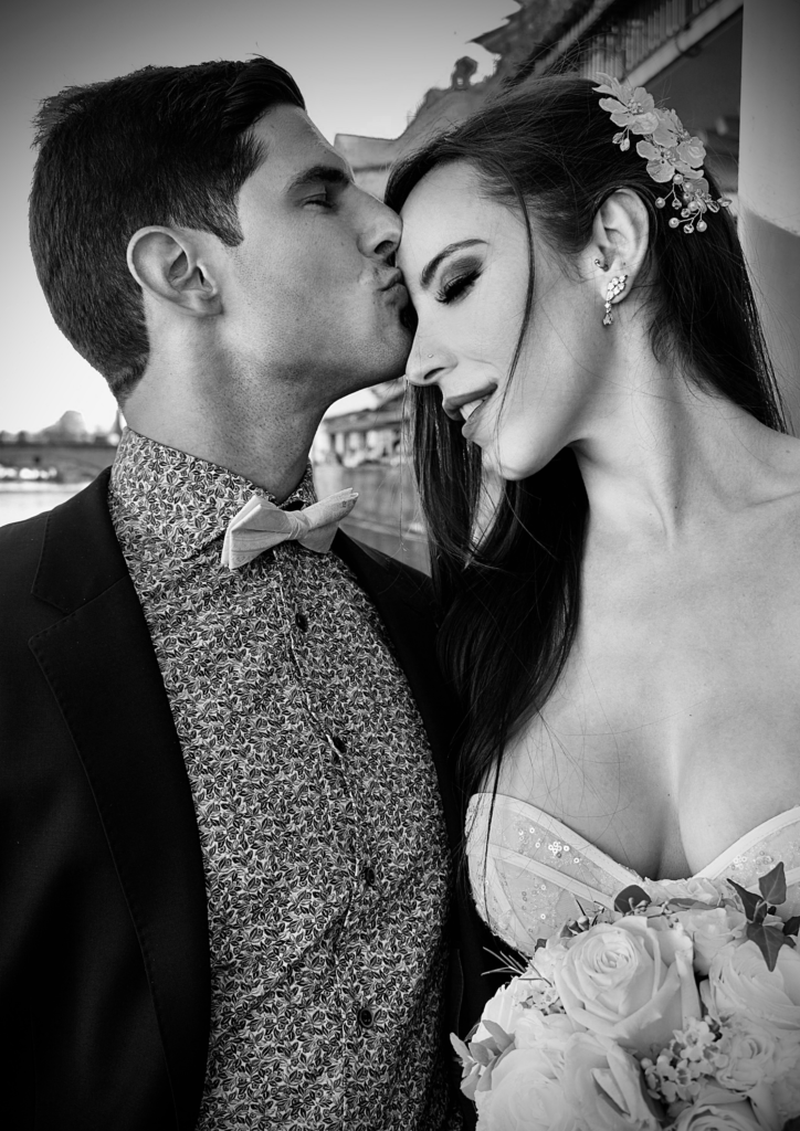 Black and white photo of a man kissing a woman’s forehead on their wedding day.