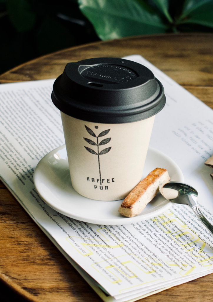 A cup of coffee on a plate next to biscotti on top of a book with highlighted text.