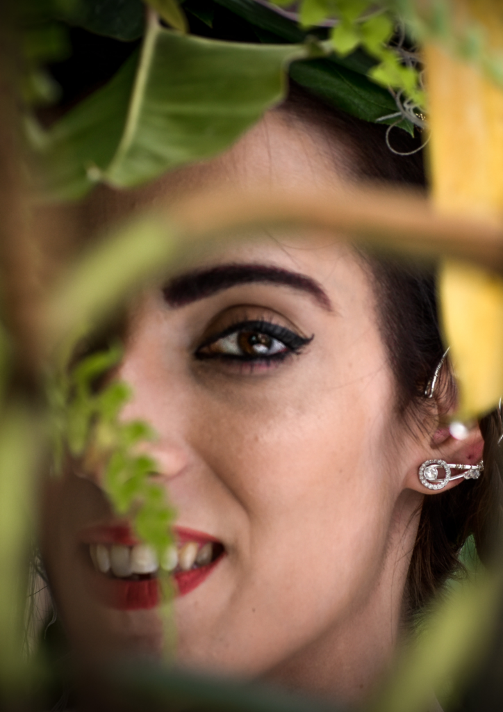 Woman smiling behind leaves with a close-up focus on her eye.